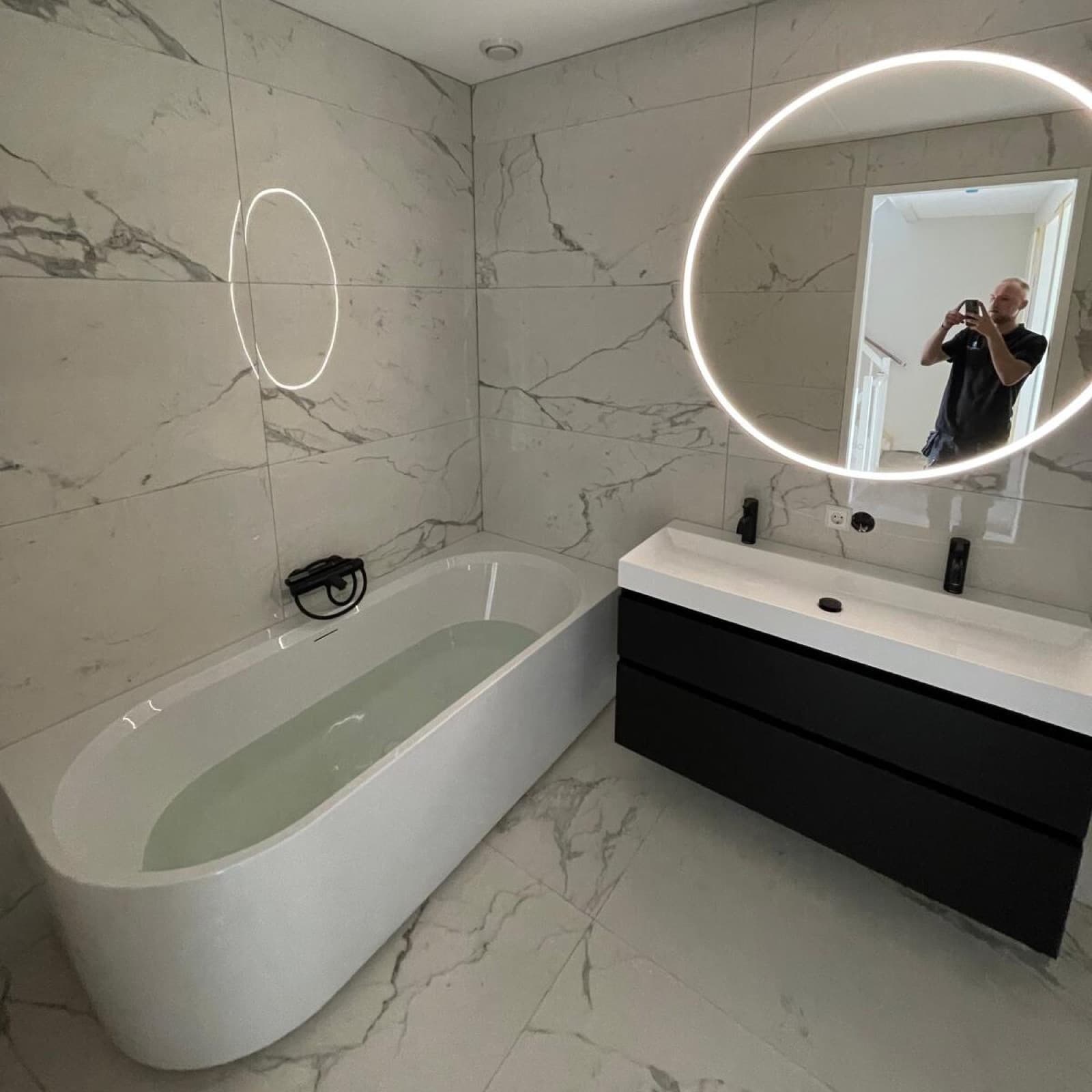 Gerenoveerde badkamer met vrijstaand ligbad, marmerlook tegels en verlichte spiegel